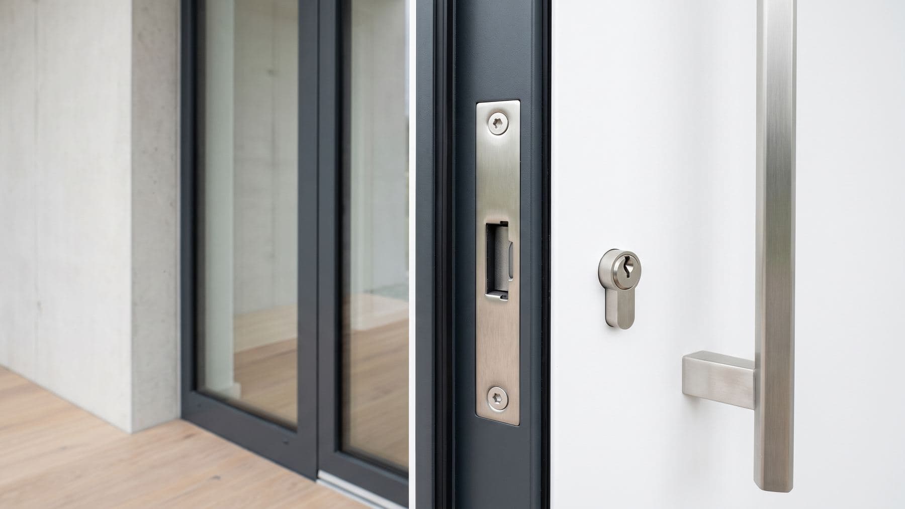 Gâche renforcée en inox neuve vissée dans le dormant aluminium anthracite d’une porte d’entrée moderne fermée