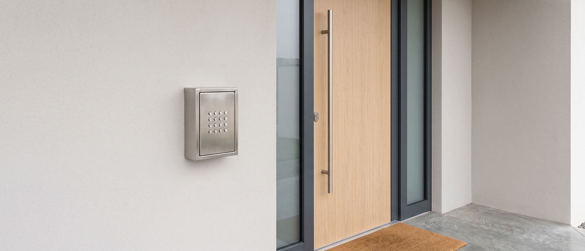 Boîte à clés murale en inox fixée près de la porte d’entrée d’un logement récent, clavier sans inscription