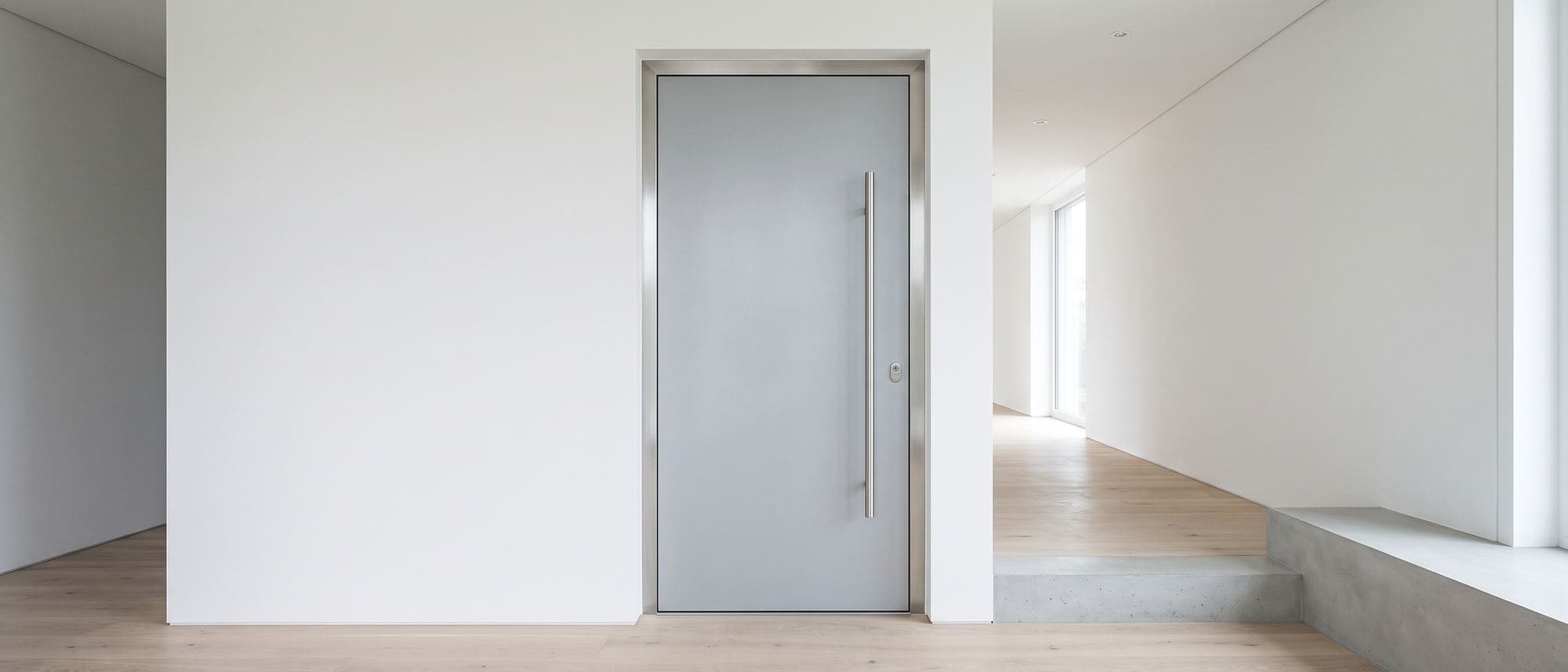 Bloc-porte blindé à panneau d’acier gris clair et huisserie inox, fermé dans une entrée contemporaine