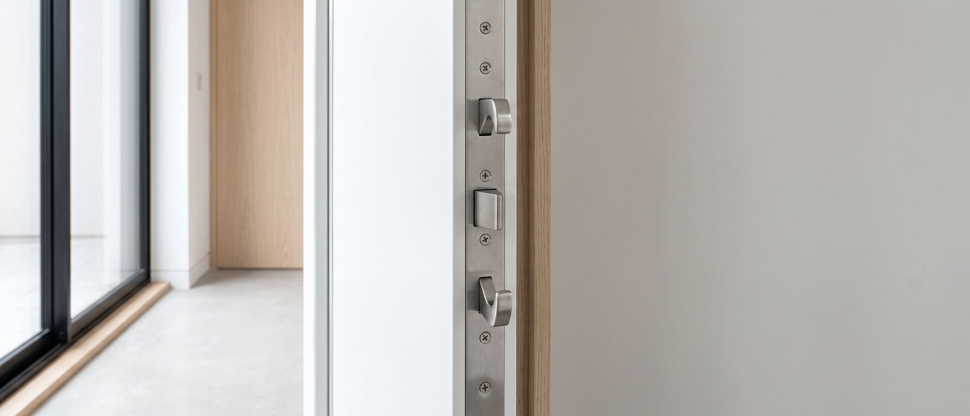 Chant d’une porte moderne ouverte montrant la têtière multipoints en inox, pêne dormant et crochets